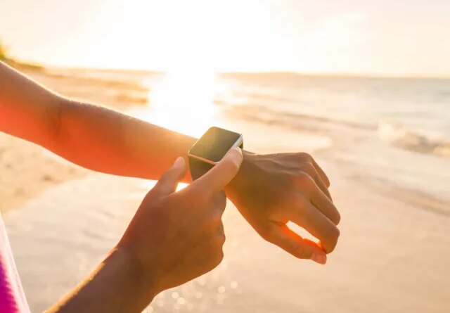 woman checking fitness tracker on the beach at sunset