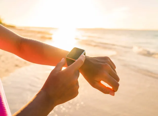 woman checking fitness tracker on the beach at sunset